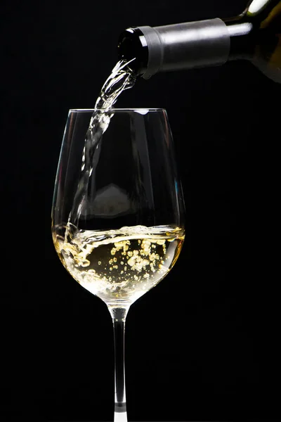 Siyah arka plandaki bardağa beyaz şarap dök. Kutlama, dezenfekte, başarı.