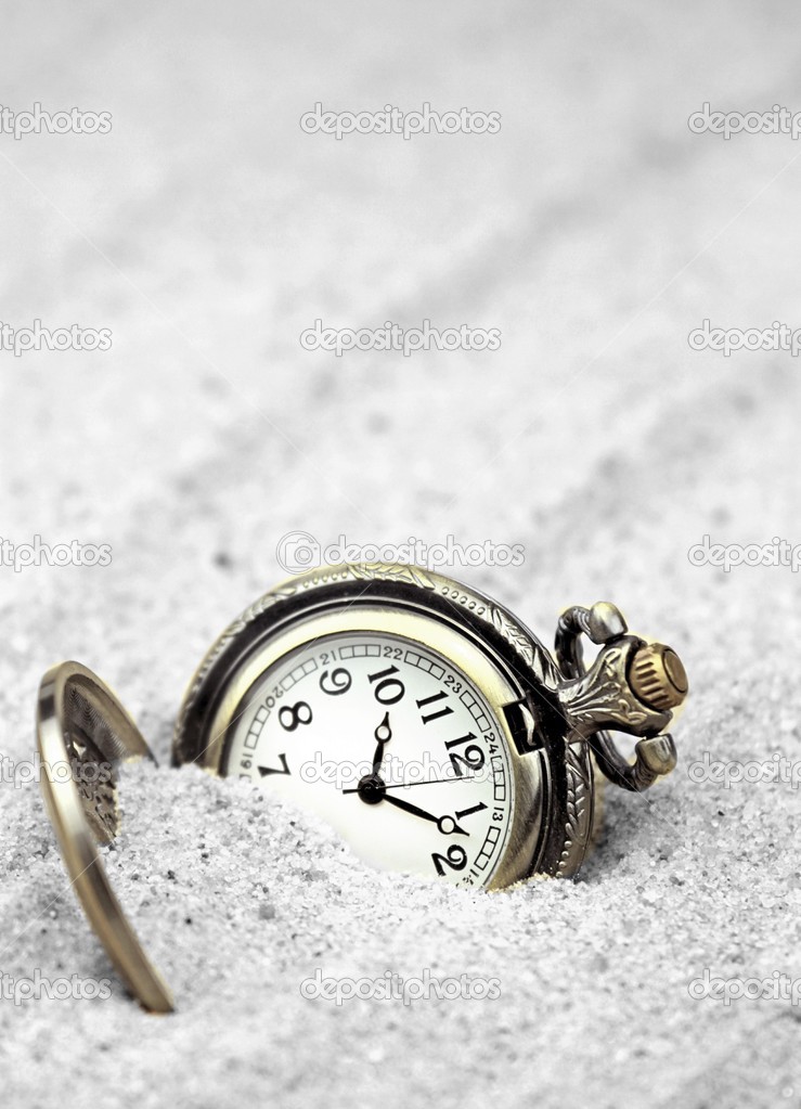 Antique pocket watch buried in sand.