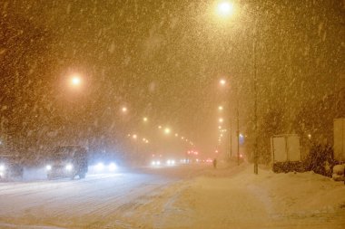 Akşamları, yoğun bir kar yağışı sırasında fenerlerle aydınlatılan ve araba kullanan şehir caddesi.