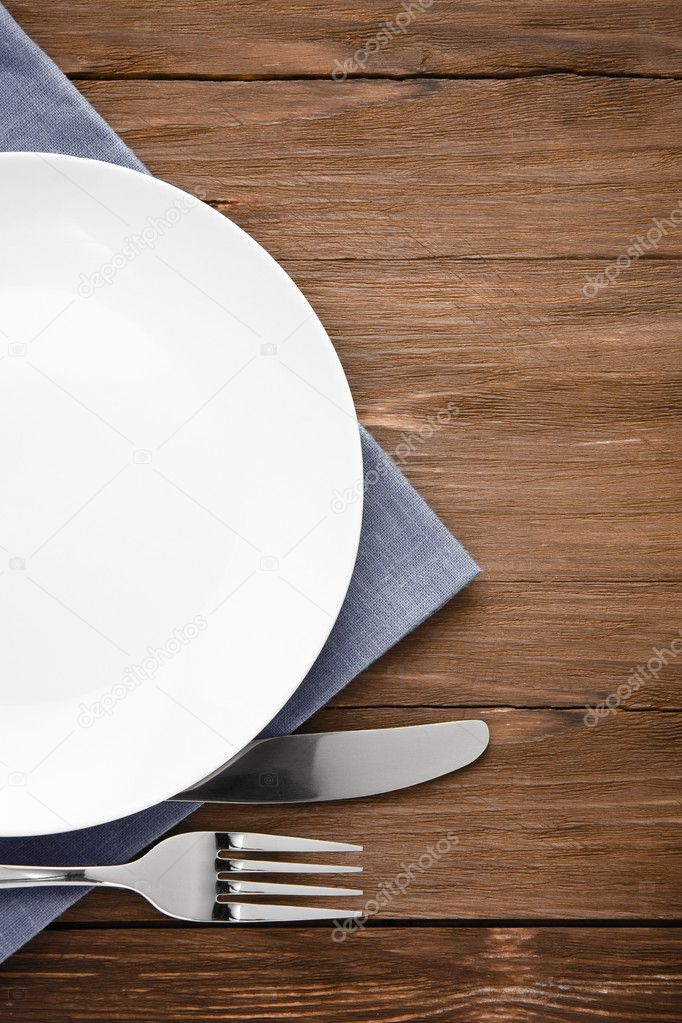 white plate, knife and fork on wood