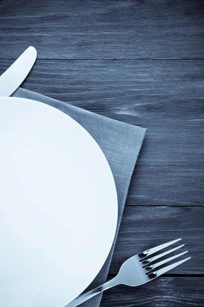 Белая тарелка, нож и вилка на дереве — стоковое фото