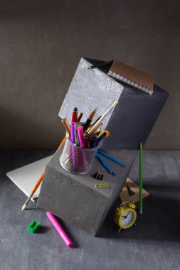 Masadaki okul konseptine geri dönelim. Beton küp arka planındaki malzeme ve aksesuarları incele
