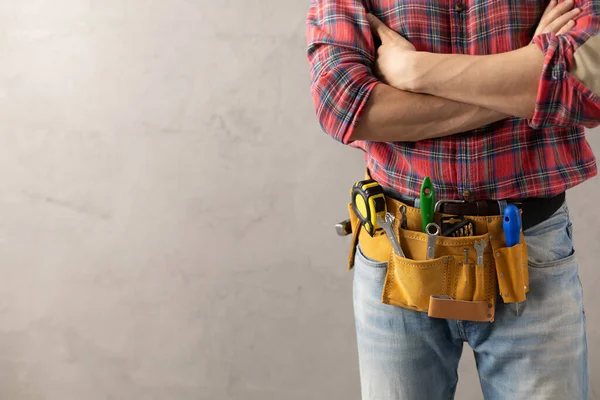 Worker man with tool belt near concrete or cement wall. Male hand and tools for house room renovation. Home renovation concept