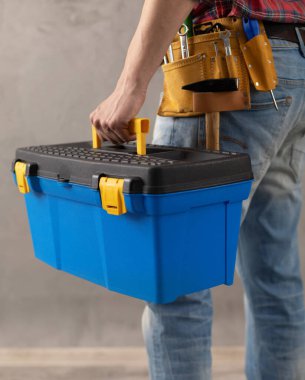 Tadilat odasındaki inşaat malzemeleri kutusunu tutan bir işçi. Erkek el ve alet çantası beton ya da beton duvarın yanında. Ev yenileme konsepti