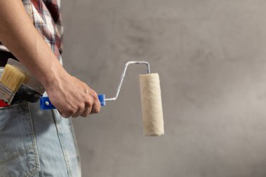 Construction worker man holding paint roller tool in house room renovation. Male hand and construction tools near concrete or plaster wall. Home renovation concept