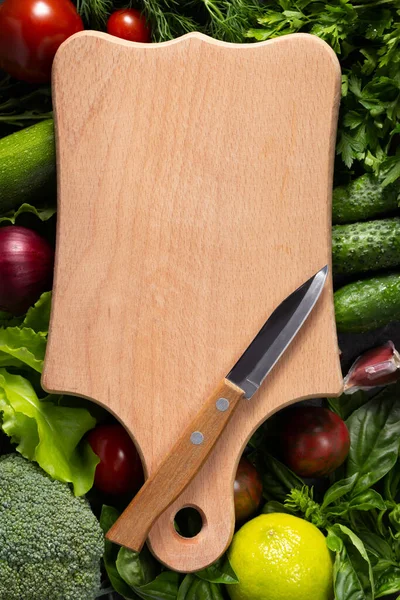 Variety of fresh vegetables and wood cutting board on table background. Cookig concept and salad ingredients at tabletop top view