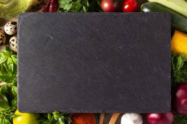 Taze sebzelerin çeşitliliği ve masa arkasında kayrak taşı. Masa başı görünümünde aşçılık konsepti ve salata malzemeleri