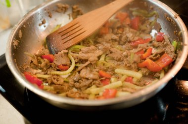Cook fries meat in a pan with vegetables.