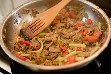Cook fries meat in a pan with vegetables.