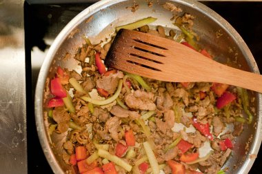 Cook fries meat in a pan with vegetables.
