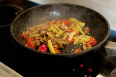 Cook fries meat in a pan with vegetables.