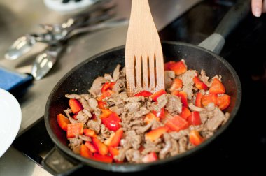 Cook fries meat in a pan with vegetables.