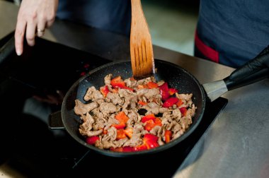 Cook fries meat in a pan with vegetables.