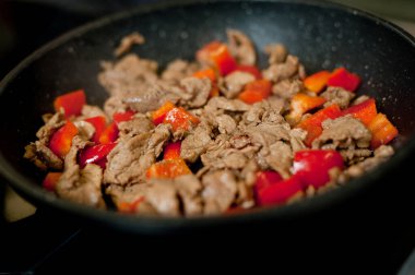 Cook fries meat in a pan with vegetables.