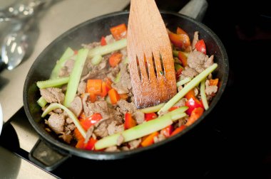 Cook fries meat in a pan with vegetables.