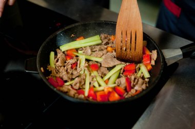 Cook fries meat in a pan with vegetables.