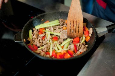 Cook fries meat in a pan with vegetables.