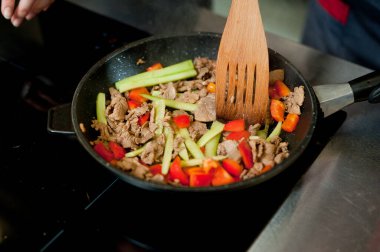 Cook fries meat in a pan with vegetables.