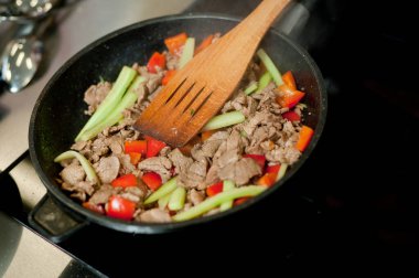 Cook fries meat in a pan with vegetables.