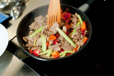Cook fries meat in a pan with vegetables.