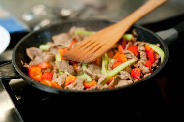 Cook fries meat in a pan with vegetables.