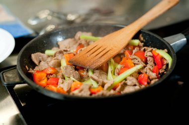 Cook fries meat in a pan with vegetables.