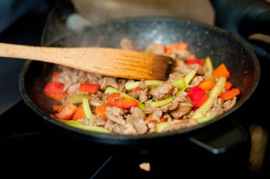 Cook fries meat in a pan with vegetables.