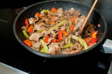 Cook fries meat in a pan with vegetables.