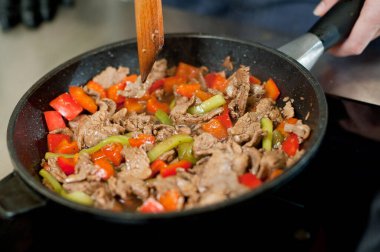 Cook fries meat in a pan with vegetables.