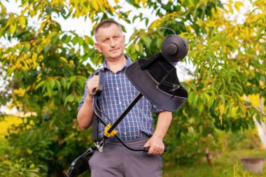 Bahçıvan elinde çim biçmek için makina tutuyor.