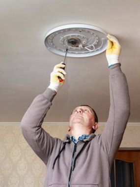 Elektrikçi odanın tavanına bir lamba, avize yerleştirir.