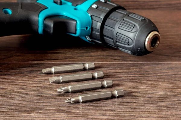 Kahverengi ahşap bir yüzeyde kablosuz tornavidanın yanındaki vidaları sıkmak için vidalar