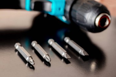 Kahverengi ahşap bir yüzeyde kablosuz tornavidanın yanındaki vidaları sıkmak için vidalar