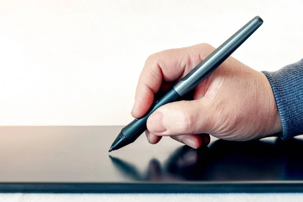 A man holds a pen, stylus, and draws with a graphics tablet