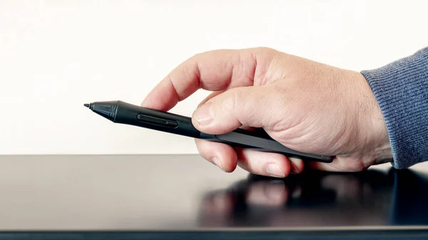 A man holds a pen in his hand, a stylus, for a graphics tablet