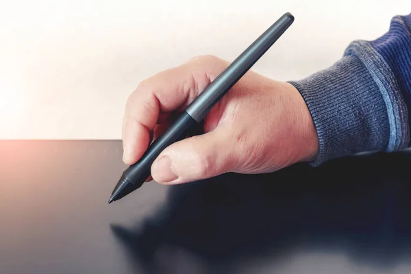 A man holds a pen, a stylus and draws with a graphics tablet