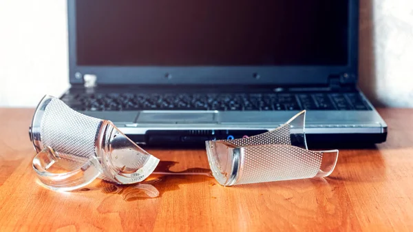 Broken glass mug with spilled coffee or tea near laptop in the office