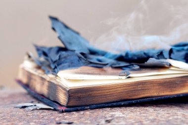 An open book with burnt charred pages and smoke on the table. Burning of banned literature clipart