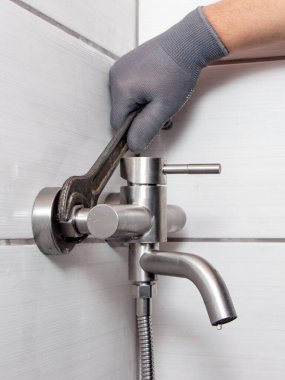 A plumber using a wrench installs a faucet in the bathroom