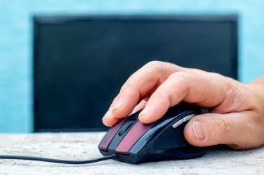 A man's hand on a computer mouse near a computer. Entering data on a computer using a mouse