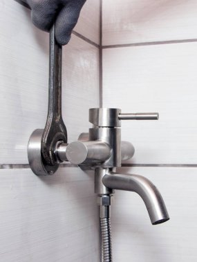 A plumber using a wrench installs a faucet in the bathroom