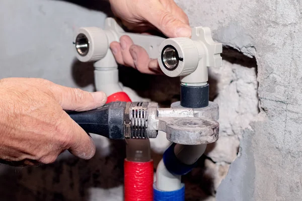 Work on the installation of heating or plumbing. The master connects plastic pipes with a soldering iron