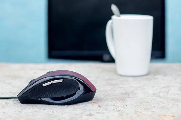 A computer mouse and a mug of tea near the computer