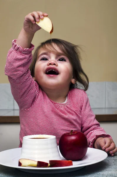 Little Jewish girl dipping apple slices into honey — Stock Photo, Image