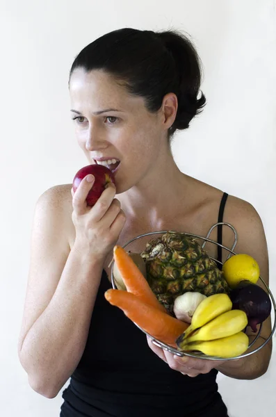 Mladá žena jí jablko a drží mísu s ovocem — Stock fotografie
