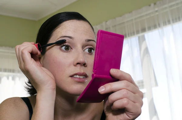 Young woman looks in mirror and applies mascara — Stock Photo, Image