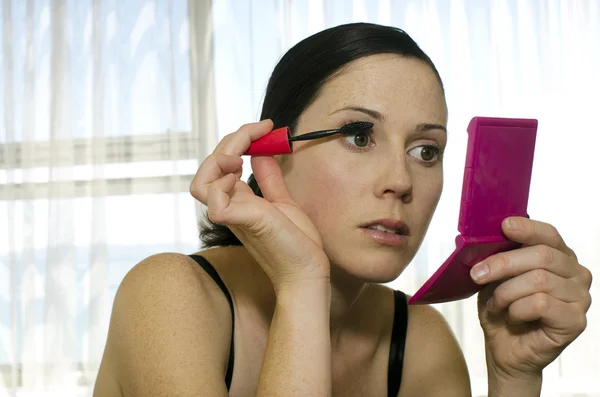 Jonge vrouw in spiegel kijkt en toepassing van mascara — Stockfoto