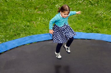 Genç kız ev arka bahçesinde trambolin üzerinde atlar. 