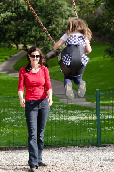 Junge Mutter schaukelt Kind auf Spielplatz — Stockfoto