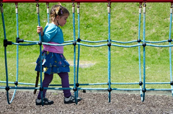 Criança atravessando ponte suspensa no parque infantil — Fotografia de Stock